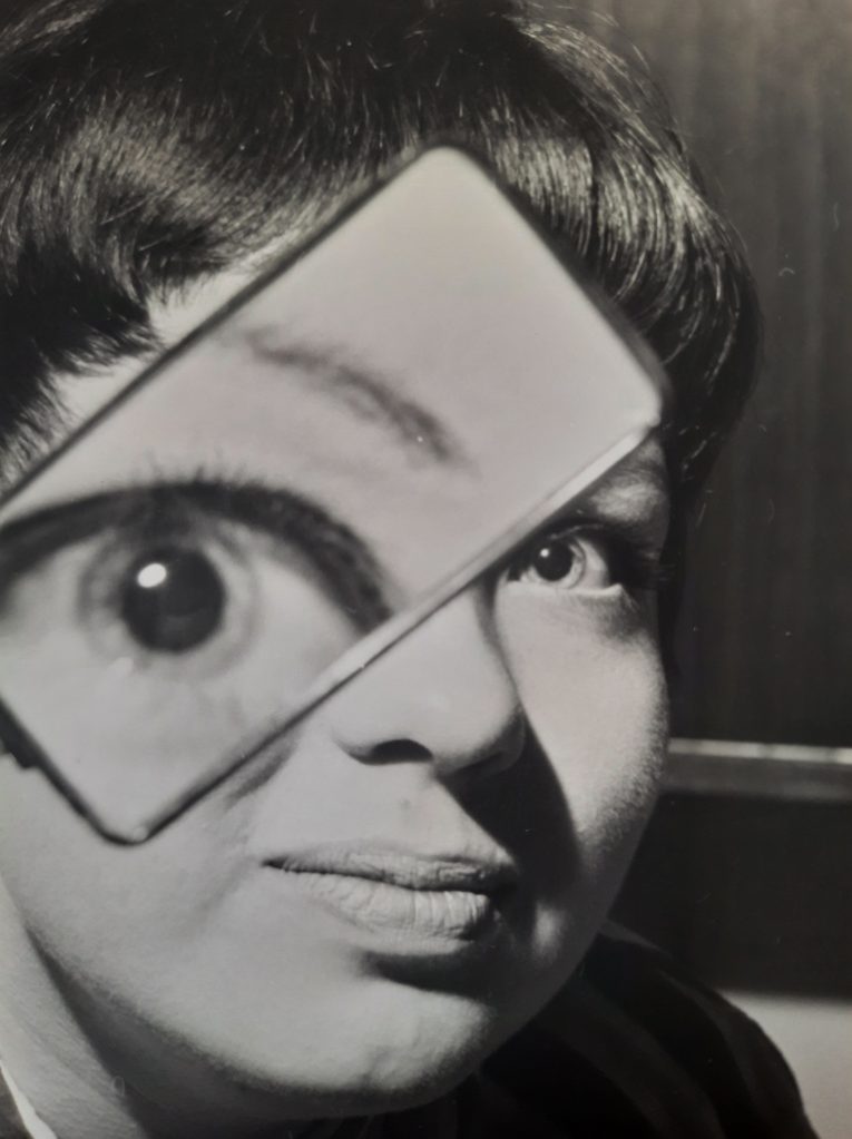 A black and white photograph of a person holding a mirror that reflects one of their eyes, creating an artistic visual effect.